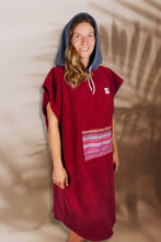 Eine Person, die einen bunten Boho Hippie Surf-Poncho mit aztekischem Muster trägt, steht an einem Strand. Der Poncho reicht bis knapp über die Knie und scheint aus einem dicken, saugfähigen Material zu bestehen. Bohemian Tribal Ethnic Patterned Colorful Beachwear Surfing Hooded Poncho Oversized Unisex Hippie-chic Festival fashion Beach accessory Mexican-inspired Southwestern Geometric Vibrant Multicolored Soft cotton Beach towel Quick-drying surfumkleide