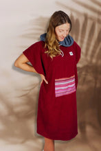 Eine Person, die einen bunten Boho Hippie Surf-Poncho mit aztekischem Muster trägt, steht an einem Strand. Der Poncho reicht bis knapp über die Knie und scheint aus einem dicken, saugfähigen Material zu bestehen. Bohemian Tribal Ethnic Patterned Colorful Beachwear Surfing Hooded Poncho Oversized Unisex Hippie-chic Festival fashion Beach accessory Mexican-inspired Southwestern Geometric Vibrant Multicolored Soft cotton Beach towel Quick-drying surfumkleide