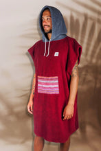 Eine Person, die einen bunten Boho Hippie Surf-Poncho mit aztekischem Muster trägt, steht an einem Strand. Der Poncho reicht bis knapp über die Knie und scheint aus einem dicken, saugfähigen Material zu bestehen. Bohemian Tribal Ethnic Patterned Colorful Beachwear Surfing Hooded Poncho Oversized Unisex Hippie-chic Festival fashion Beach accessory Mexican-inspired Southwestern Geometric Vibrant Multicolored Soft cotton Beach towel Quick-drying surfumkleide
