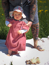 Ein Baby sitzt am Strand und trägt einen farbenfrohen Surfponcho mit einem aztekisch inspirierten Boho-Muster. Der Poncho besteht aus einem weichen, saugfähigen Material, das das Baby nach dem Schwimmen warm und trocken hält. Das lebendige und mehrfarbige Muster weist ethnische Details auf, die ihm ein Hippie-Chic-Feeling verleihen. Der Surfponcho hat eine Kapuze, um den Kopf des Babys vor Wind zu schützen, sodass er bis zu den Knien des Babys vollständig bedeckt ist. Boho hippie aztek