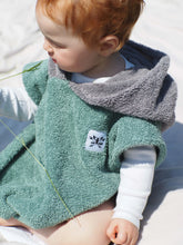 Ein Baby sitzt am Strand und trägt einen farbenfrohen Surfponcho mit einem aztekisch inspirierten Boho-Muster. Der Poncho besteht aus einem weichen, saugfähigen Material, das das Baby nach dem Schwimmen warm und trocken hält. Das lebendige und mehrfarbige Muster weist ethnische Details auf, die ihm ein Hippie-Chic-Feeling verleihen. Der Surfponcho hat eine Kapuze, um den Kopf des Babys vor Wind zu schützen, sodass er bis zu den Knien des Babys vollständig bedeckt ist. Boho hippie aztek