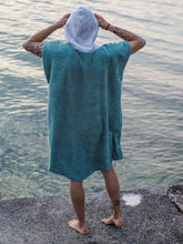 Eine Person, die einen bunten Boho Hippie Surf-Poncho mit aztekischem Muster trägt, steht an einem Strand. Der Poncho reicht bis knapp über die Knie und scheint aus einem dicken, saugfähigen Material zu bestehen. Bohemian Tribal Ethnic Patterned Colorful Beachwear Surfing Hooded Poncho Oversized Unisex Hippie-chic Festival fashion Beach accessory Mexican-inspired Southwestern Geometric Vibrant Multicolored Soft cotton Beach towel Quick-drying surfumkleide