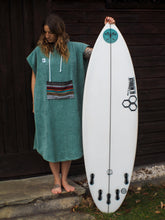 Eine Person, die einen bunten Boho Hippie Surfponcho mit aztekischem Muster trägt, steht an einem Strand. Der Poncho reicht bis knapp über die Knie und scheint aus einem dicken, saugfähigen Material zu bestehen. Bohemian Tribal Ethnic Patterned Colorful Beachwear Surfing Hooded Poncho Oversized Unisex Hippie-chic Festival fashion Beach accessory Mexican-inspired Southwestern Geometric Vibrant Multicolored Soft cotton Beach towel Quick-drying surfumkleide