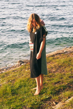 A person wearing a colorful boho hippie surf poncho with an aztec pattern stands on a beach. The poncho comes down to just above the knees and appears to be made out of a thick, absorbent material. Bohemian Tribal Ethnic Patterned Colorful Beachwear Surfing Hooded Poncho Oversized Unisex Hippie-chic Festival fashion Beach accessory Mexican-inspired Southwestern Geometric Vibrant Multicolored Soft cotton Beach towel Quick-drying surf changing room