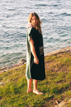 A person wearing a colorful boho hippie surf poncho with an aztec pattern stands on a beach. The poncho comes down to just above the knees and appears to be made out of a thick, absorbent material. Bohemian Tribal Ethnic Patterned Colorful Beachwear Surfing Hooded Poncho Oversized Unisex Hippie-chic Festival fashion Beach accessory Mexican-inspired Southwestern Geometric Vibrant Multicolored Soft cotton Beach towel Quick-drying surf changing room