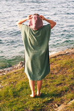 A person wearing a colorful boho hippie surf poncho with an aztec pattern stands on a beach. The poncho comes down to just above the knees and appears to be made out of a thick, absorbent material. Bohemian Tribal Ethnic Patterned Colorful Beachwear Surfing Hooded Poncho Oversized Unisex Hippie-chic Festival fashion Beach accessory Mexican-inspired Southwestern Geometric Vibrant Multicolored Soft cotton Beach towel Quick-drying surf changing room